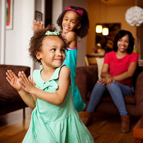 Mother looking at happy daughters dancing in living room