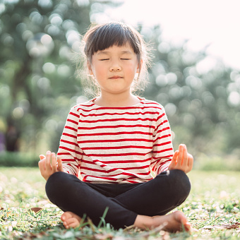 Little girl practising yoga meditation on the lawn joyfully
