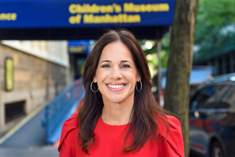 Brown haired woman in a red shirt in front of a building