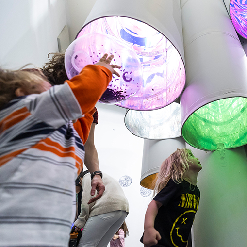 children standing under and looking up into white tubes with colors in them