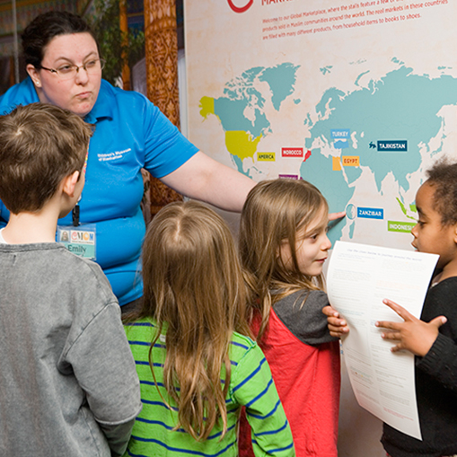woman in blue shirt instructing group of children in front of a map