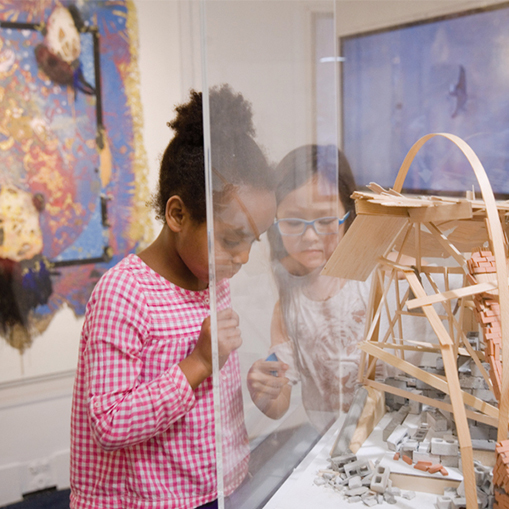 two girls looking at a piece of art behind glass