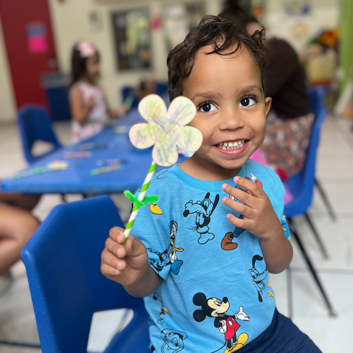male child with blue shirt with disney characters holding an arts and crafts flower