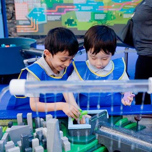 two male children wearing smocks and playing at a table with water features