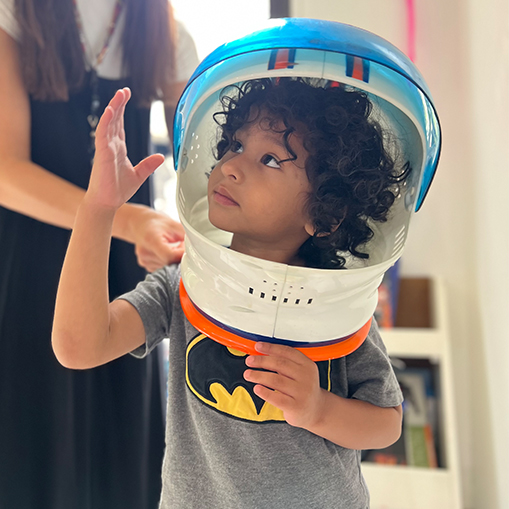 boy in batman shirt holding arm up and wearing plastic space helmet