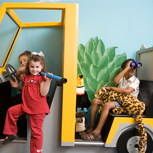 children in an open-sided yellow safari vehicle, one holding an animal in her lap