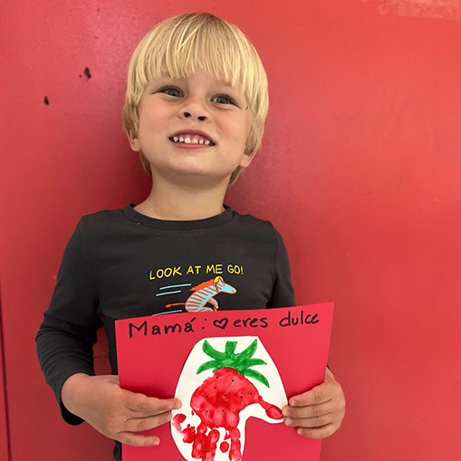 blonde boy holding red piece of paper with spanish writing