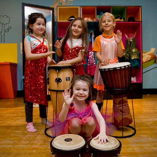 group of female children playing drums with hands in sparkly dresses