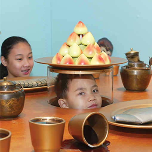 A Child peeks out from under a plate of food in the