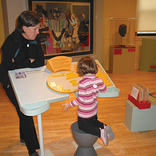 Child exploring the Art of Romare Bearden exhibit with woman behind large book
