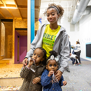 woman standing with two girls holding kazoos