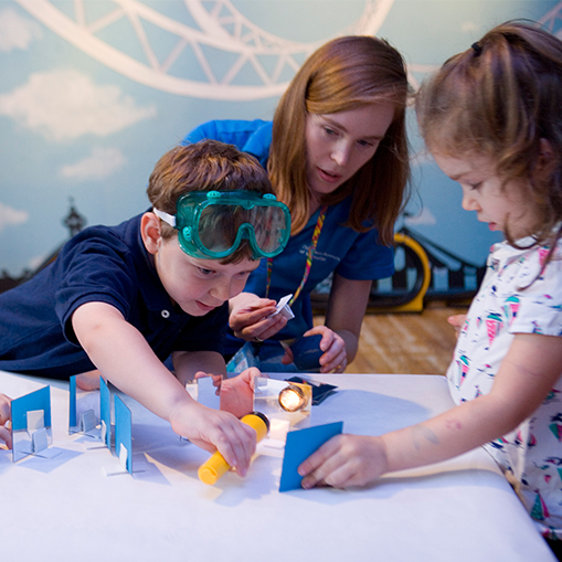 children with adult conducting science experiment by holding flashlight at small mirror
