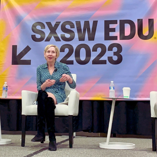 blonde woman sitting in a chair in front of a banner that reads