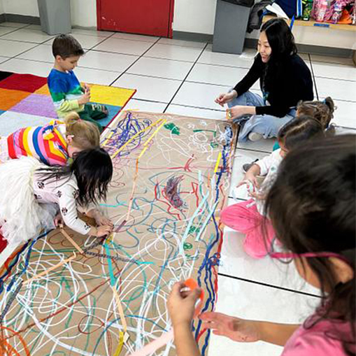 woman and children sitting on the floor and drawing on a brown piece of paper