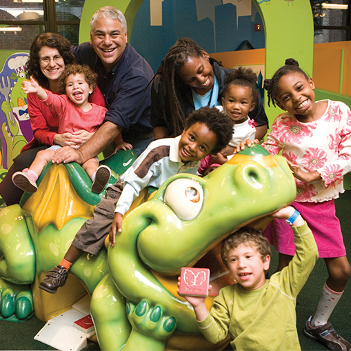 a group of children and adults sitting on a big green dragon