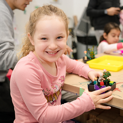 little girl smiling and holding a piece of art she made