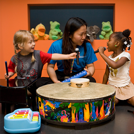 woman with a child on either side playing the drums