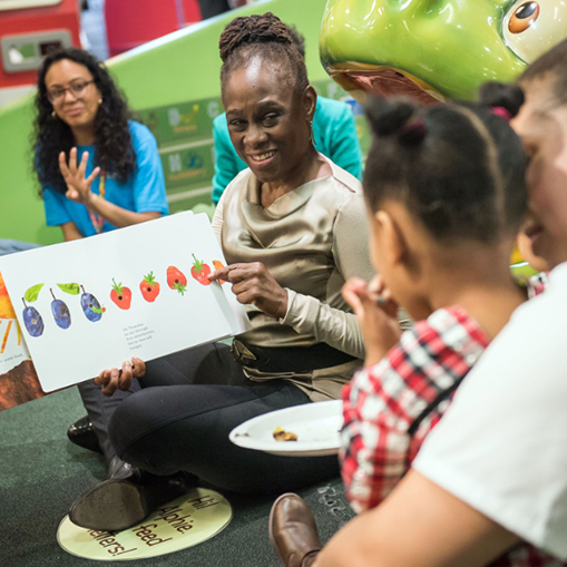 woman reading book to mother and child with another woman in the background