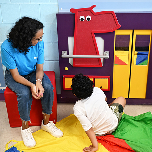 woman in blue shirt playing with child who is sitting on the ground