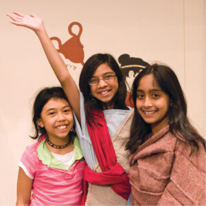 Three girls pose together and one raises her arm enthusiastically.