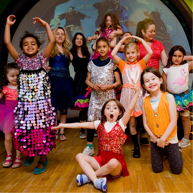 A group of kids dressed up in pretend play dance clothing smile for together.