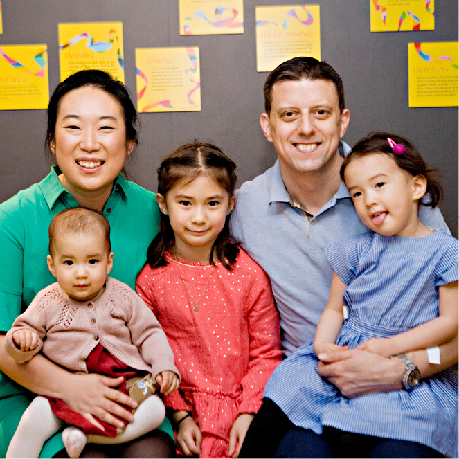 A family of five sits together and smiles.