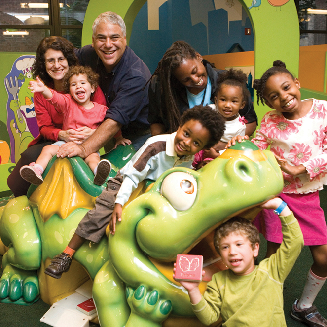 A group of kids and parents sit on Alphie, the talking dragron in the PalyWorks exhibit.