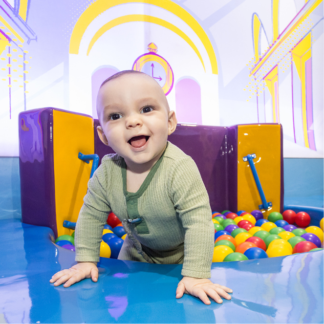A baby happily smiles in in a colorful ball put in the Superpowered Metropolis exhibit.