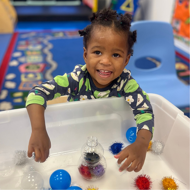 Girl smiles as she plays with colorful pom poms