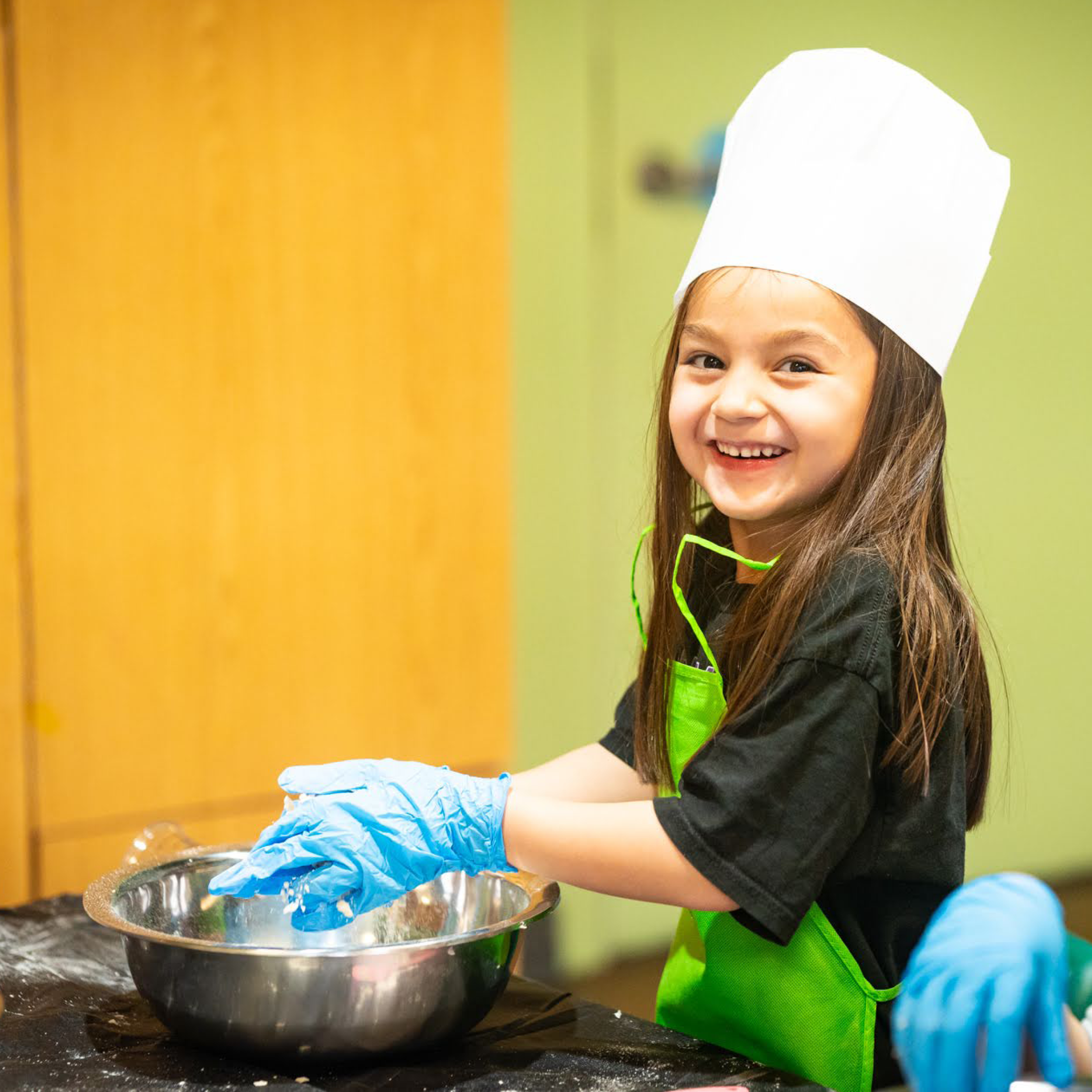 Child smiles as she mixes food in a bowl.