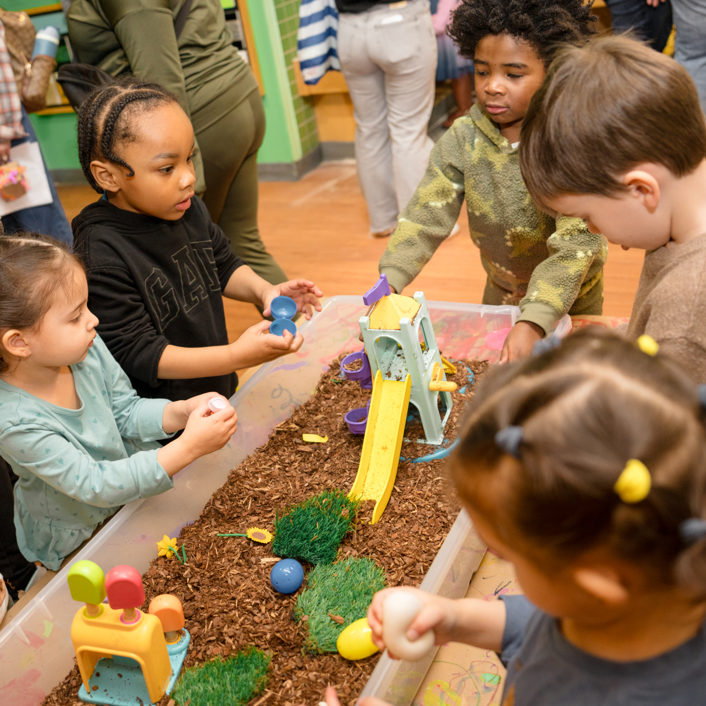 Kids play a sensory bin that includes earth, plants, plants, and other nature based materials.
