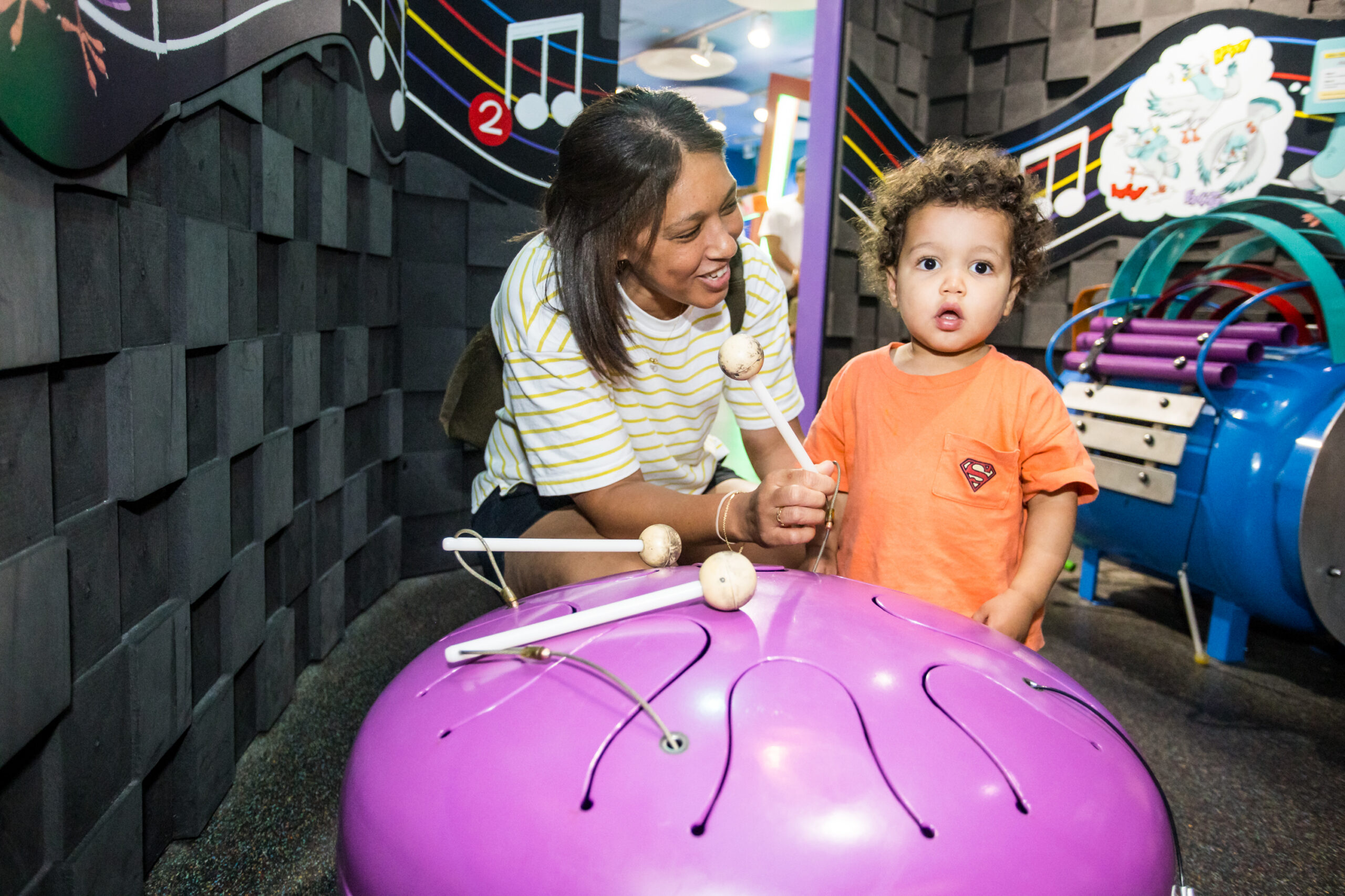 Young woman and toddler child at interactive drum toy in a children's museum exhibit