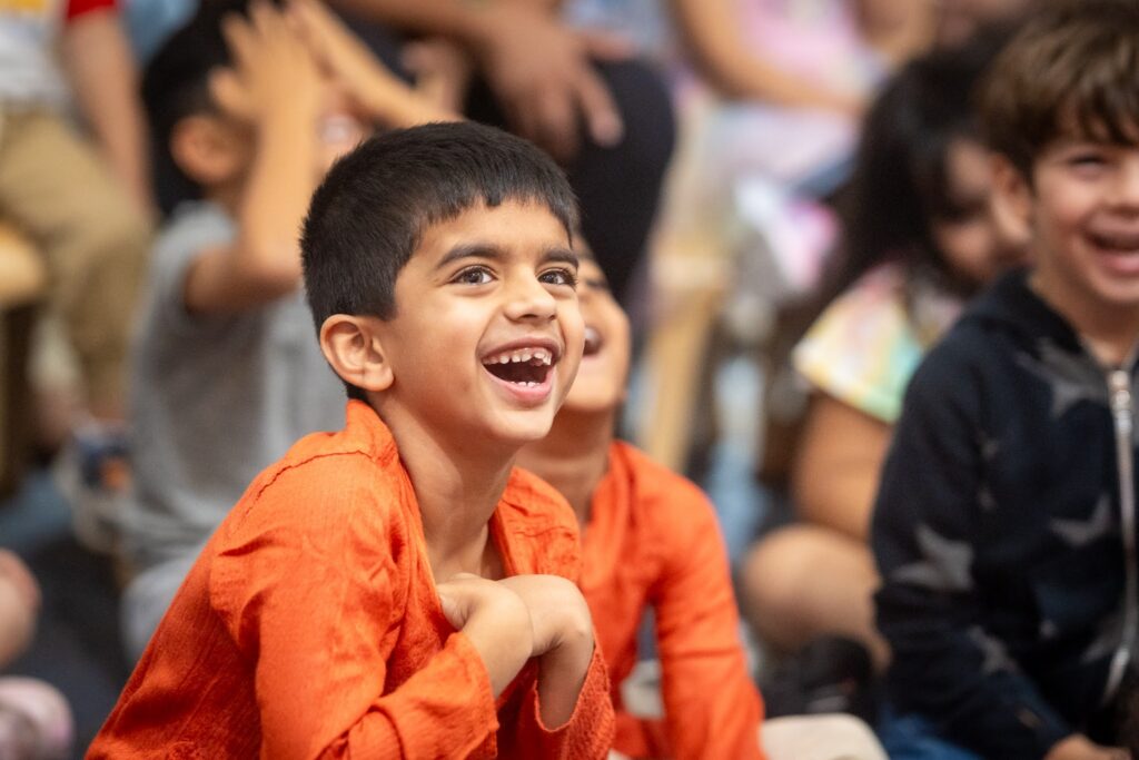 One smiling laughing boy in focus, with additional smiling laughing children behind him