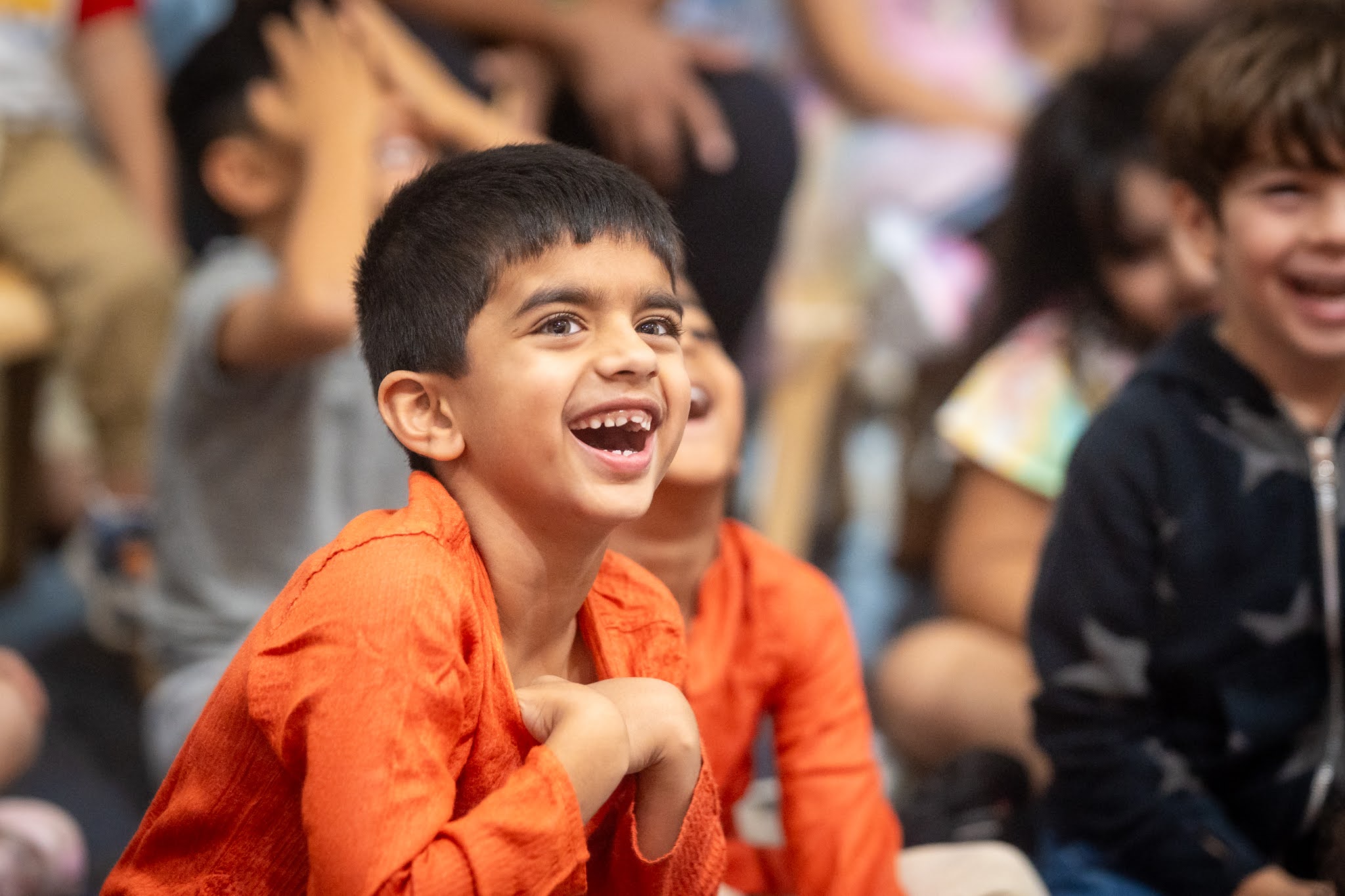 One smiling laughing boy in focus, with additional smiling laughing children behind him