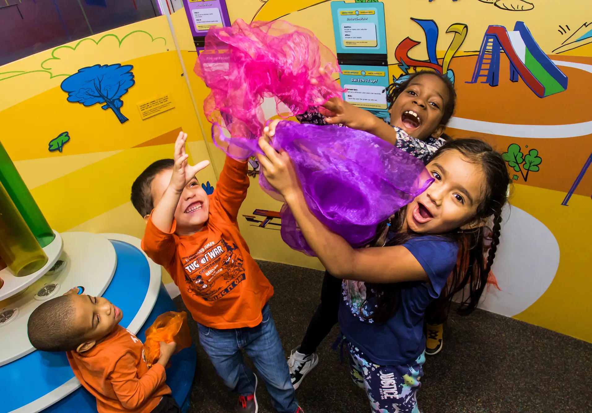 Four smiling children playing with fabric together.