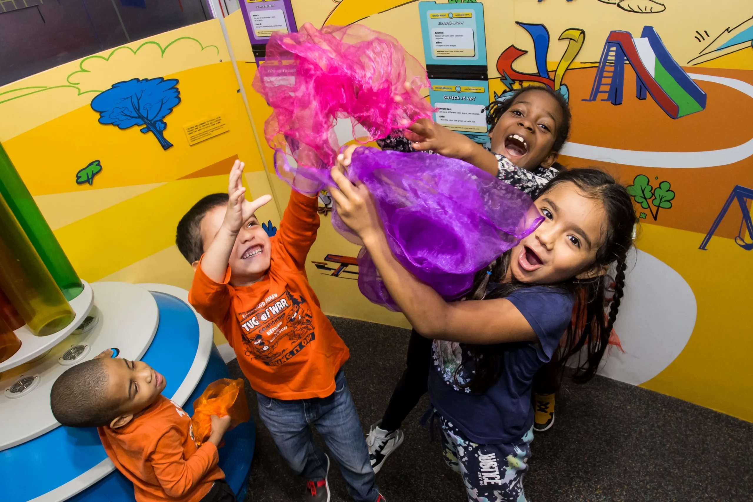 Four smiling children appear to be playing with fabric together