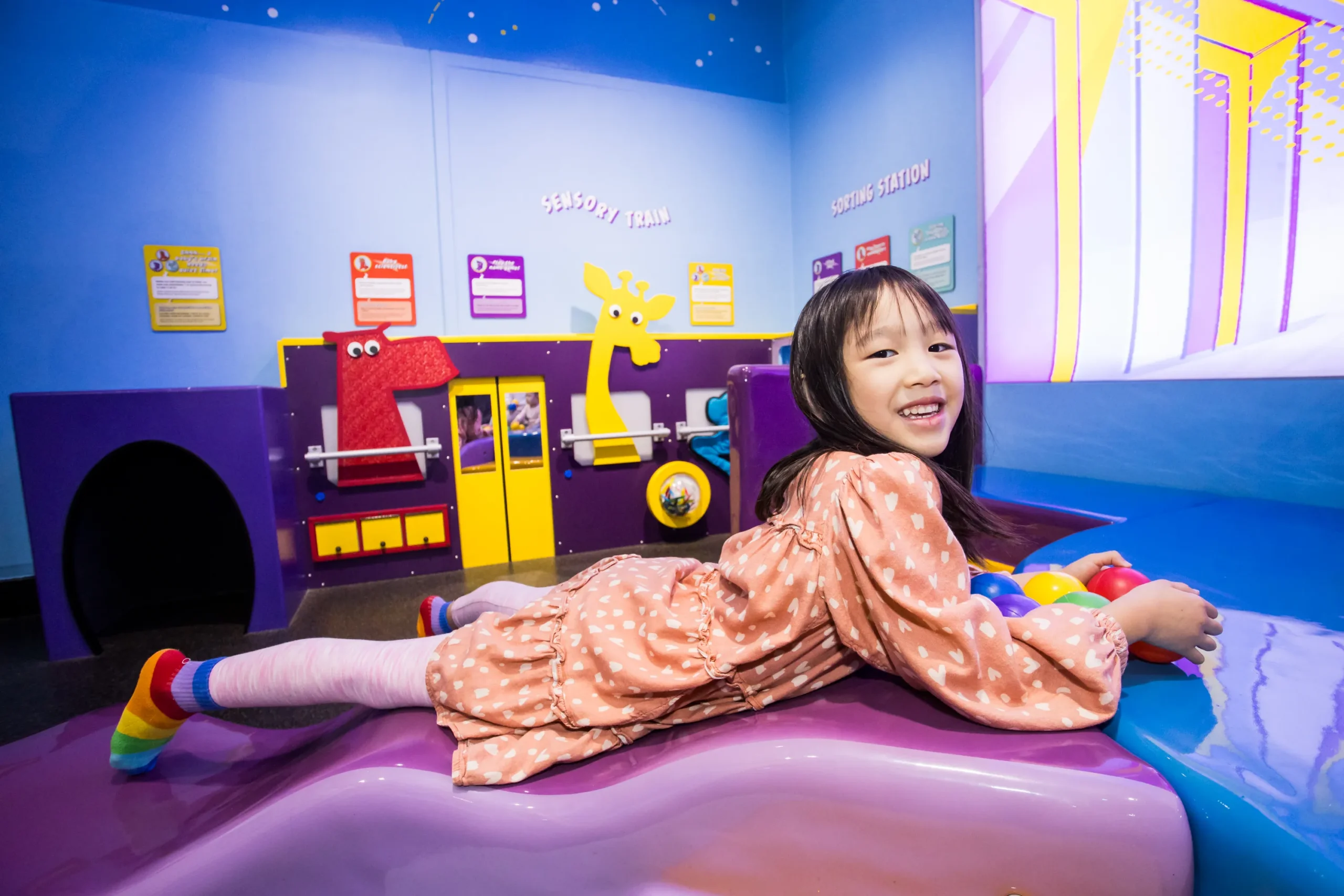 A young child lies down on an exhibit at Children's Museum of Manhattan, and holds a colorful group of balls