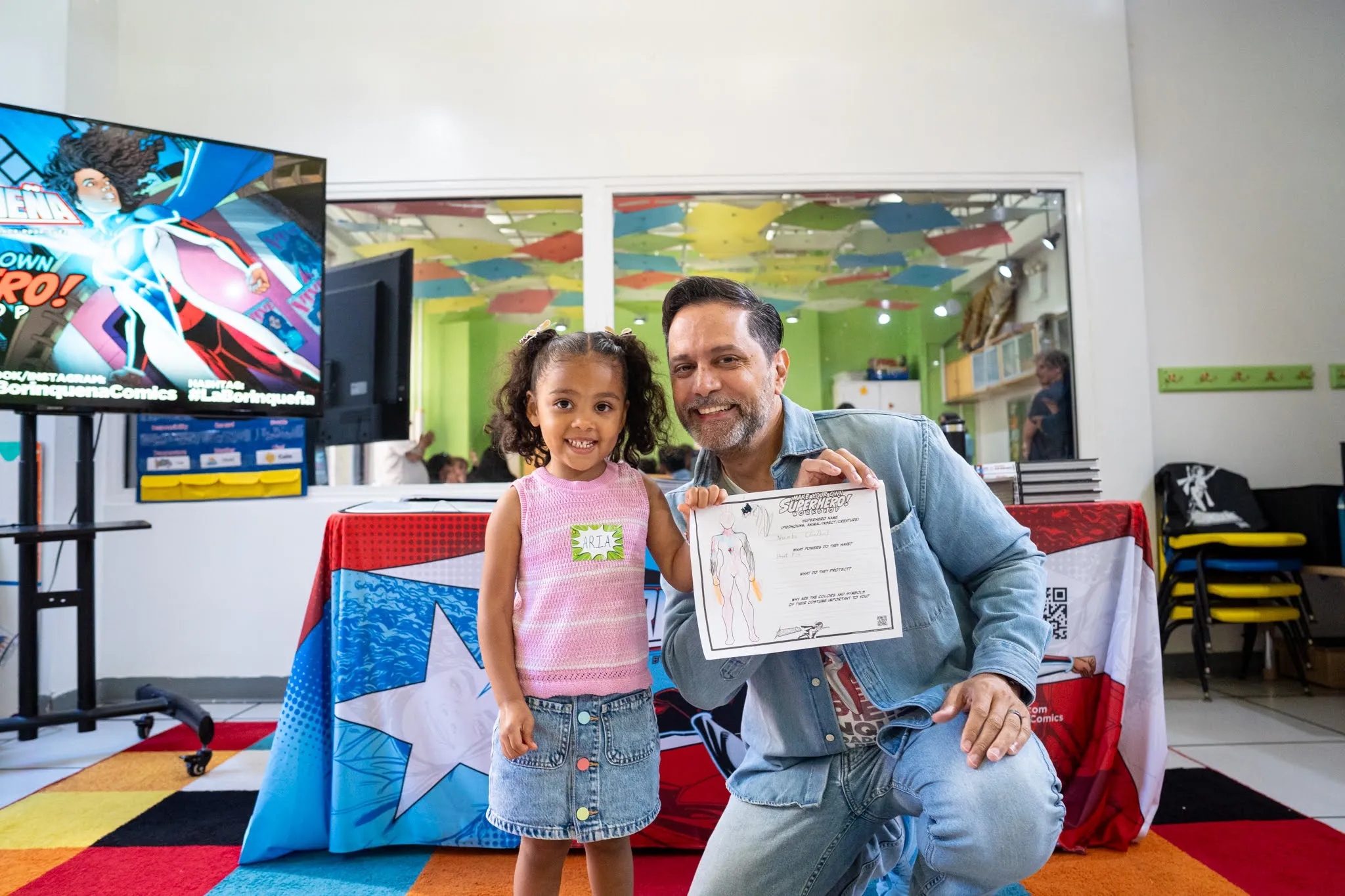 A young child and adult man both hold a certificate that says "Superhero!"