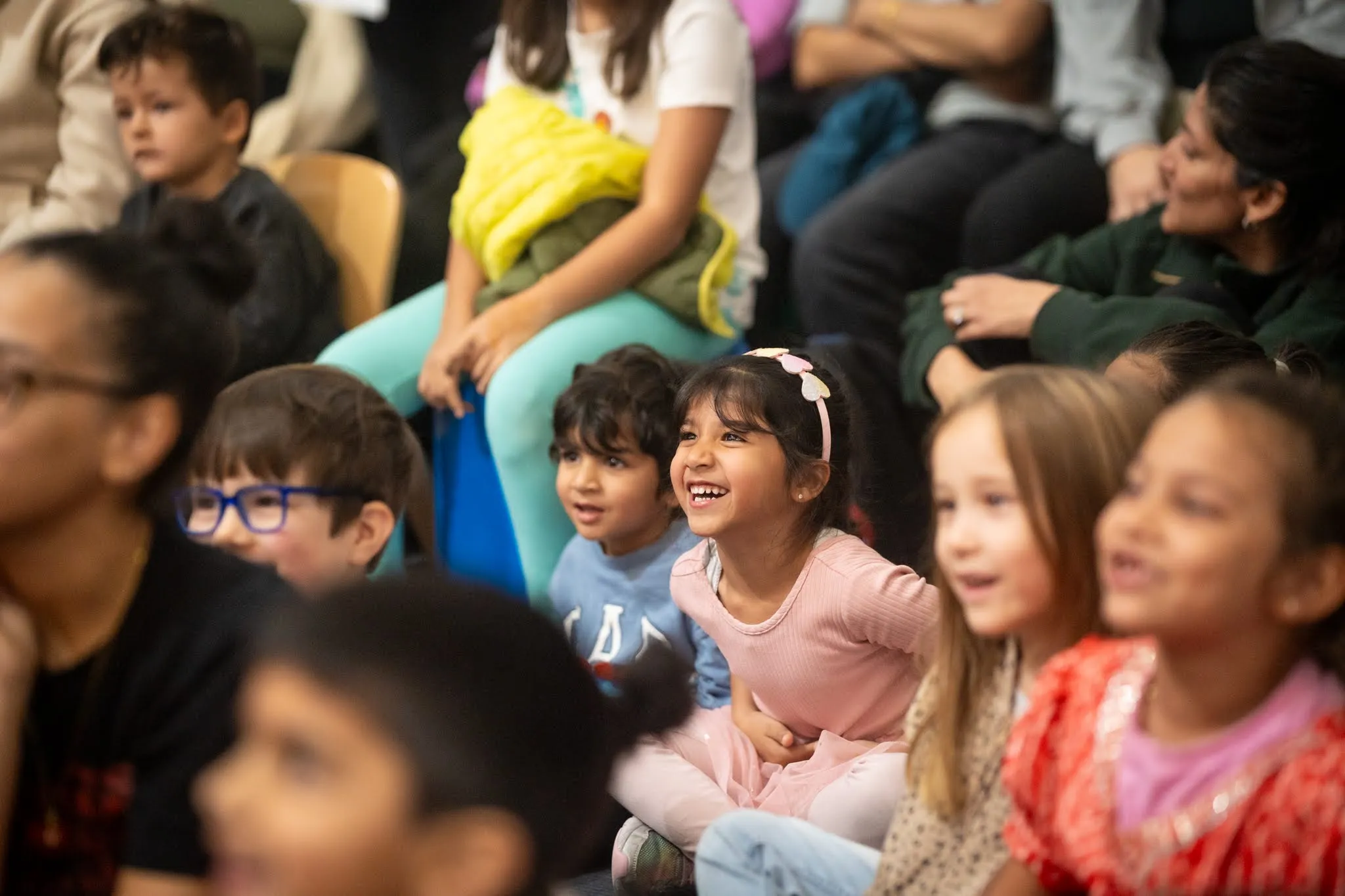 A group of small children, with two in-focus at the center of the photo, smiling at something happening off-camera