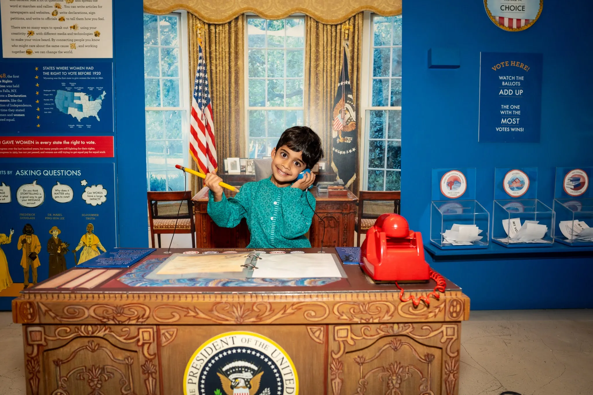 A young child sits at a reproduction of the USA's Oval Office in an exhibit at the Children's Museum of Manhattan.