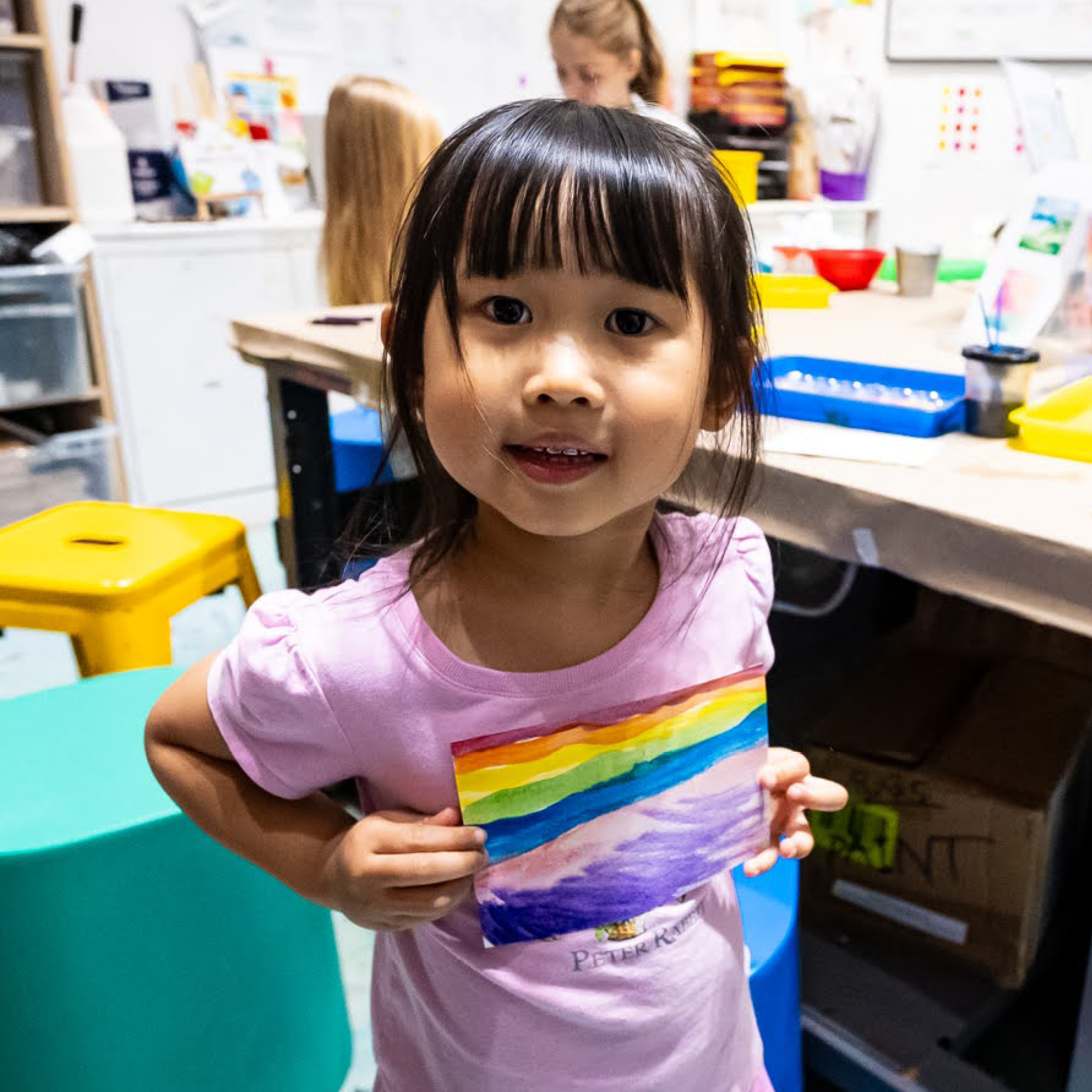Child holds up a rainbow flag that they painted.