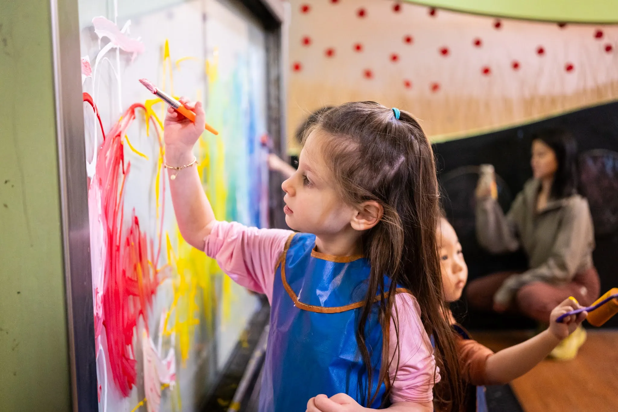 A young child paints with red paint on a wall.