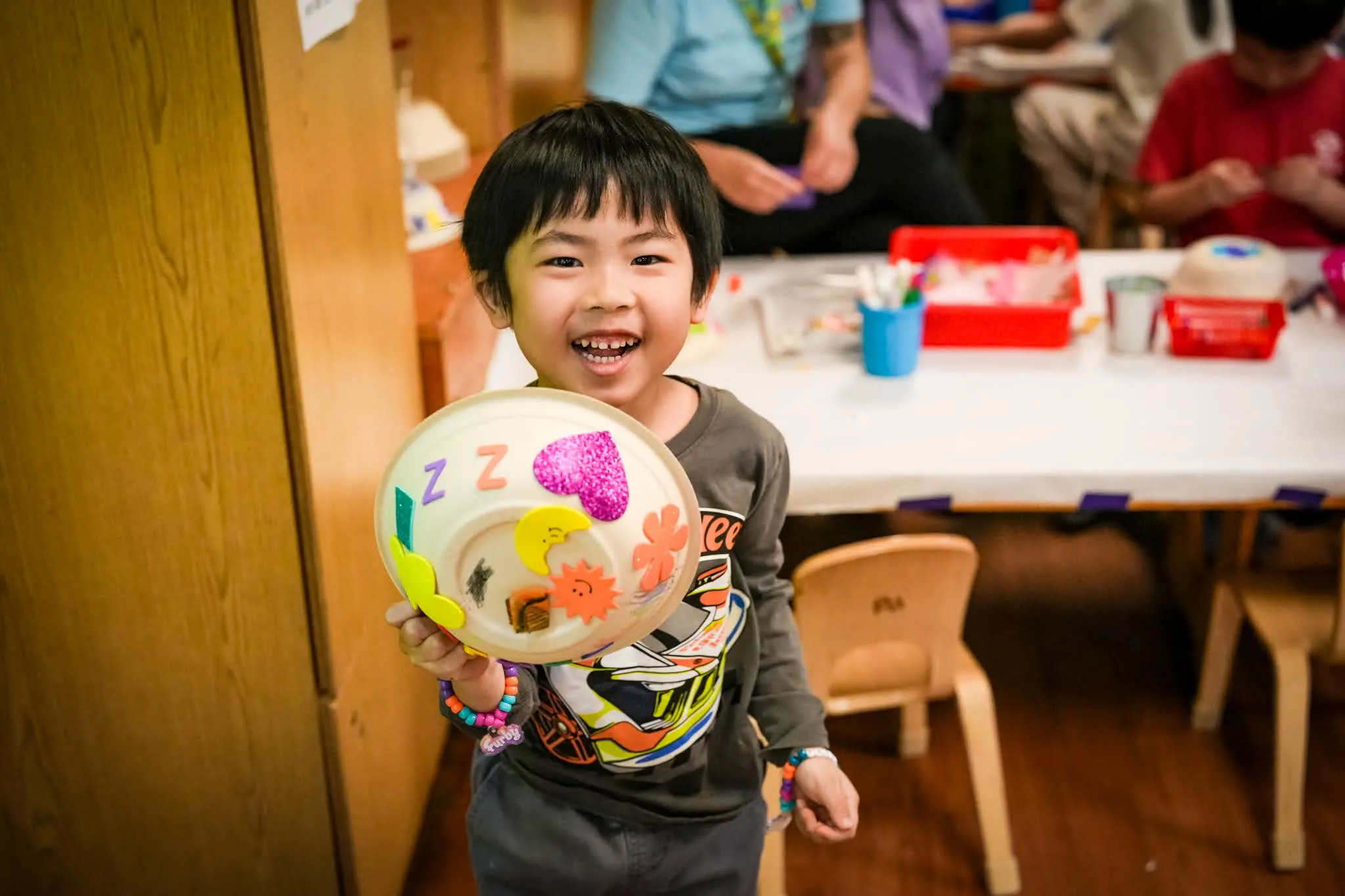 A smiling child shows off a craft to the camera.