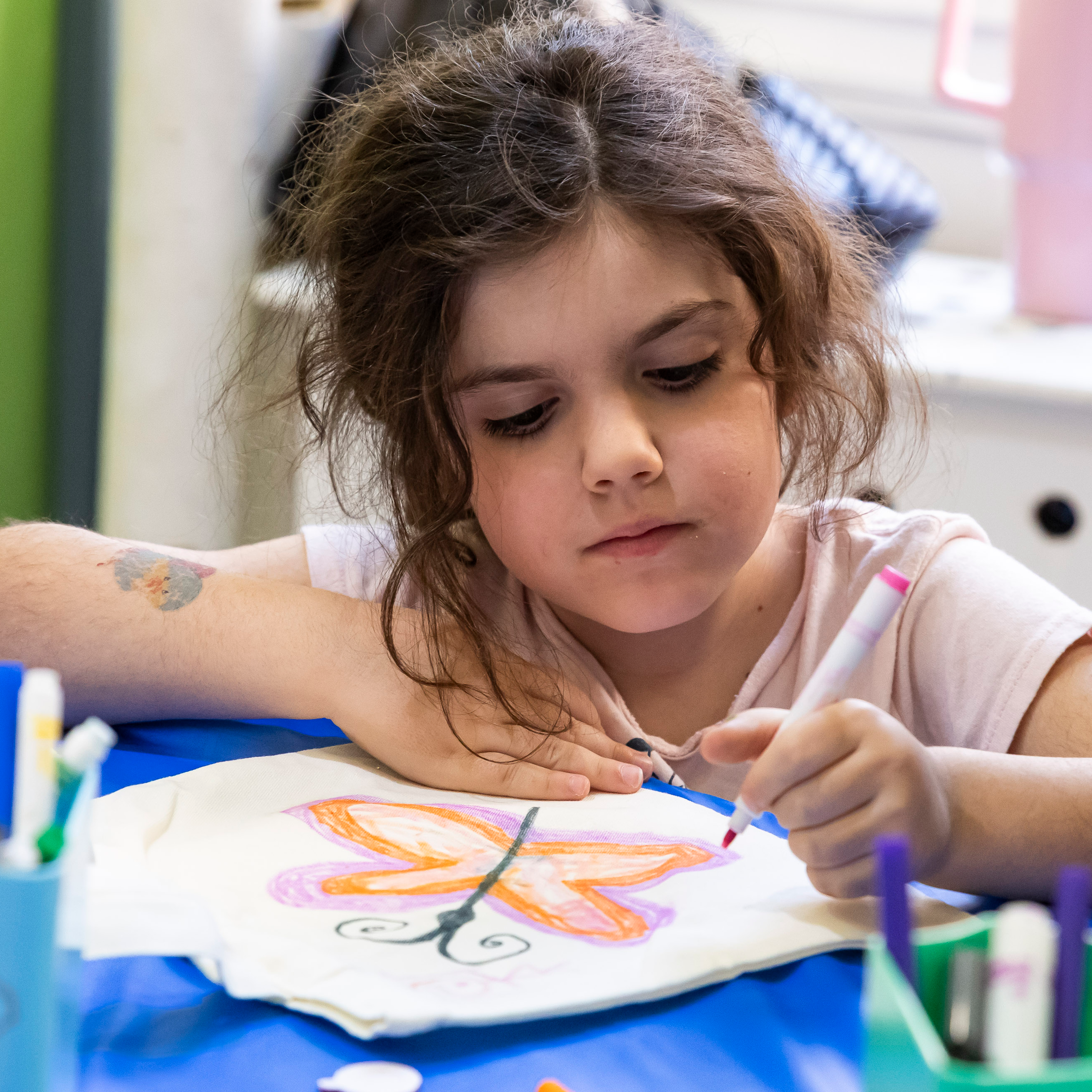 Child decorates a tote bag with a colorful butterfly.