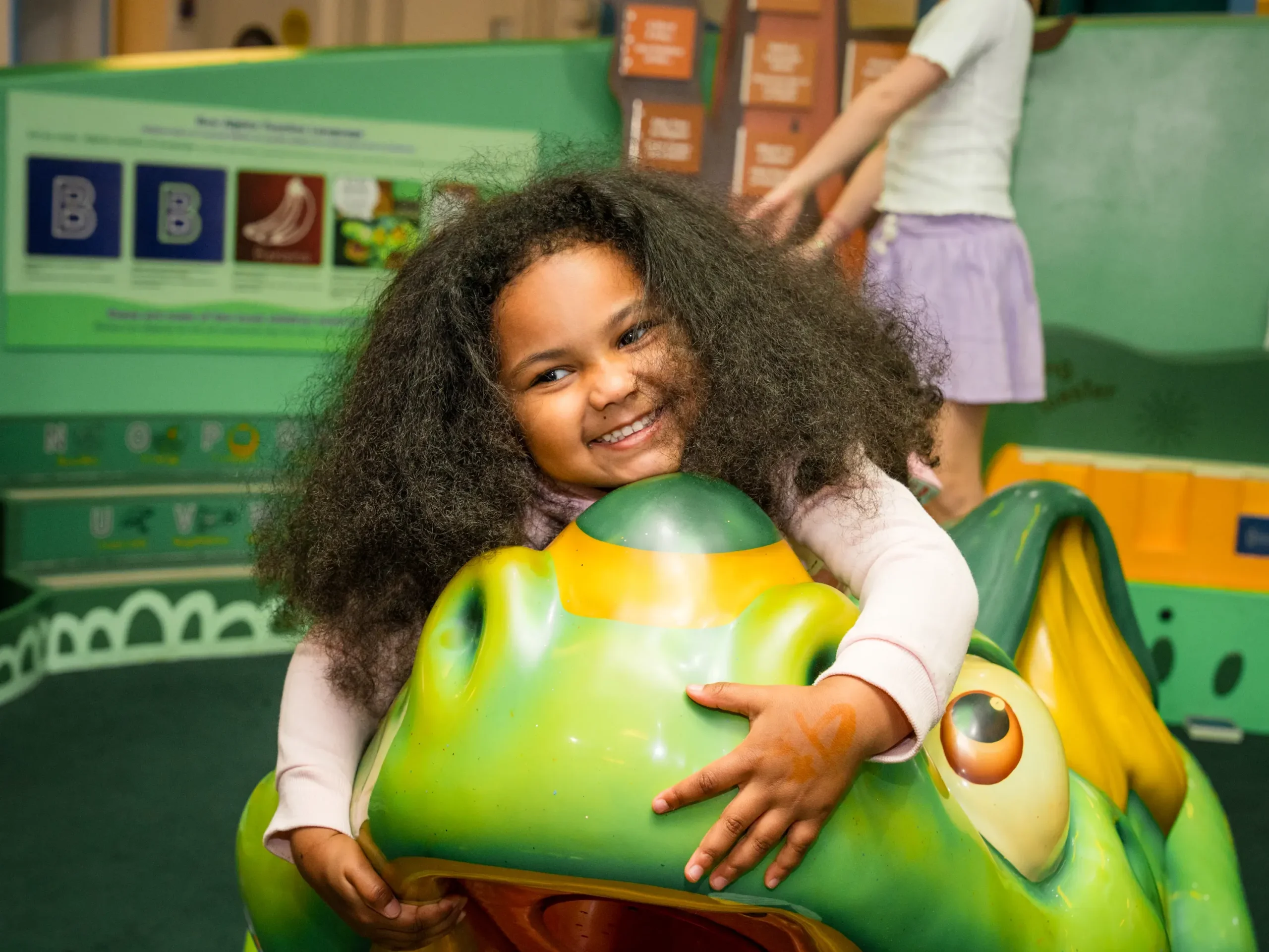 A child smiles while embracing a figure of a dragon--Alfie, the unofficial mascot of Children's Museum of Manhattan