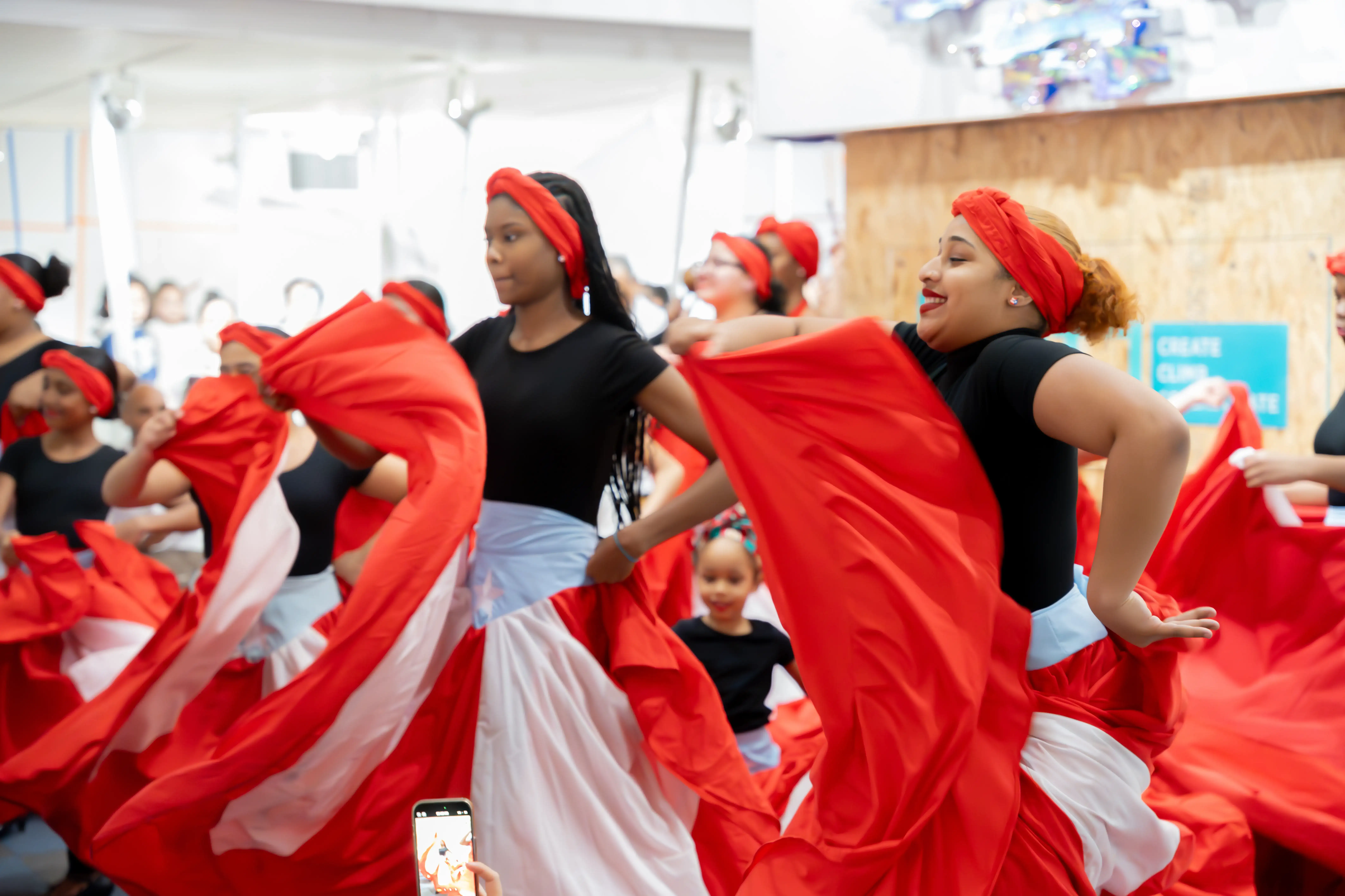 A mid-dance action shot features two of a group of dancers, twirling bright red skirts as they dance.