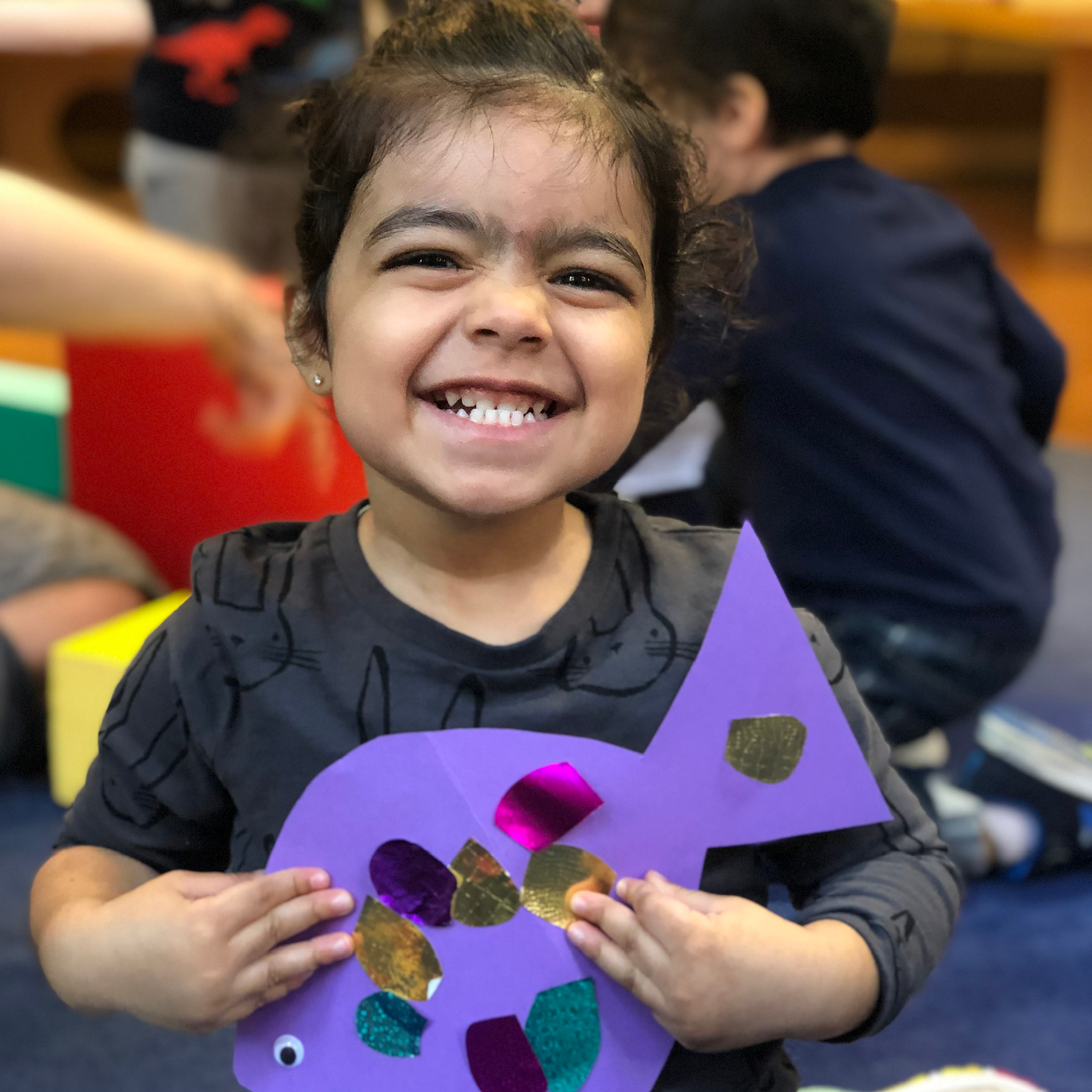 Kid smiles holding a handmade fish art project