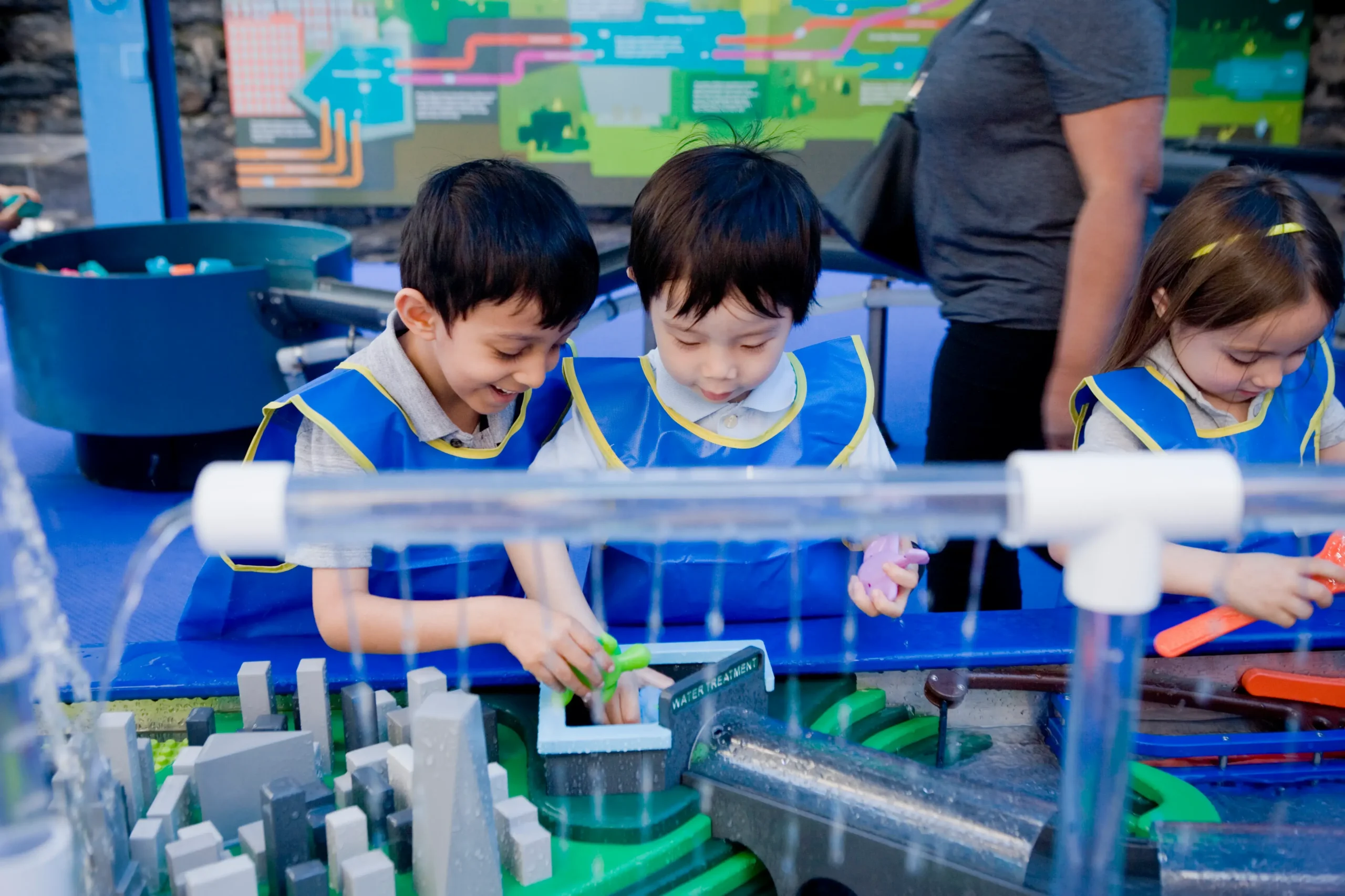 Three small children play at a water table. They all wear matching blue smocks.