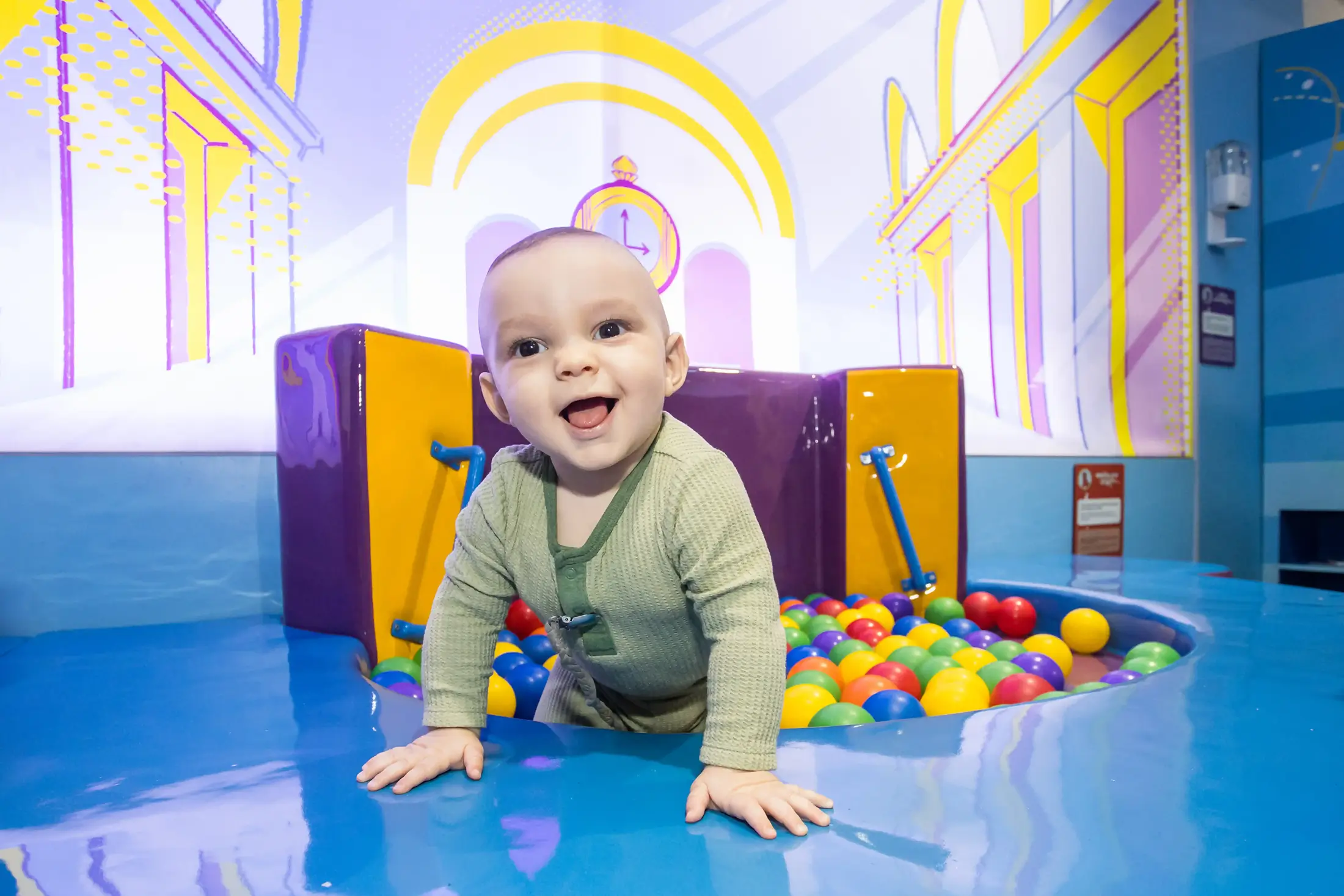 A young infant pulls himself out of a colorful pit of toy balls at a museum exhibit
