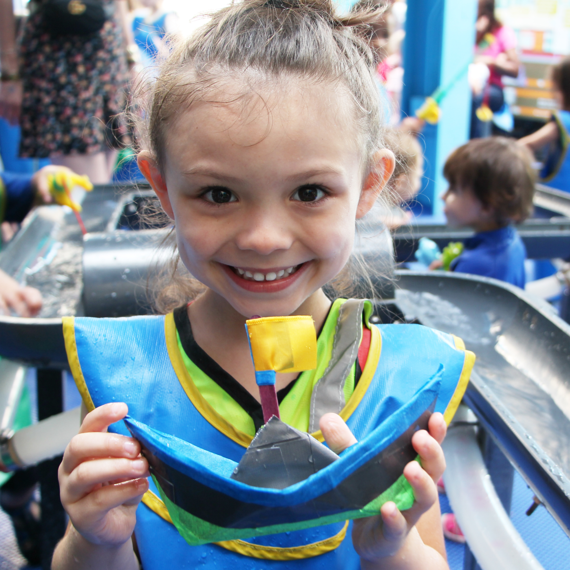 Child stands in the Dynamic H2O exhibit and holds up a handmade boat.